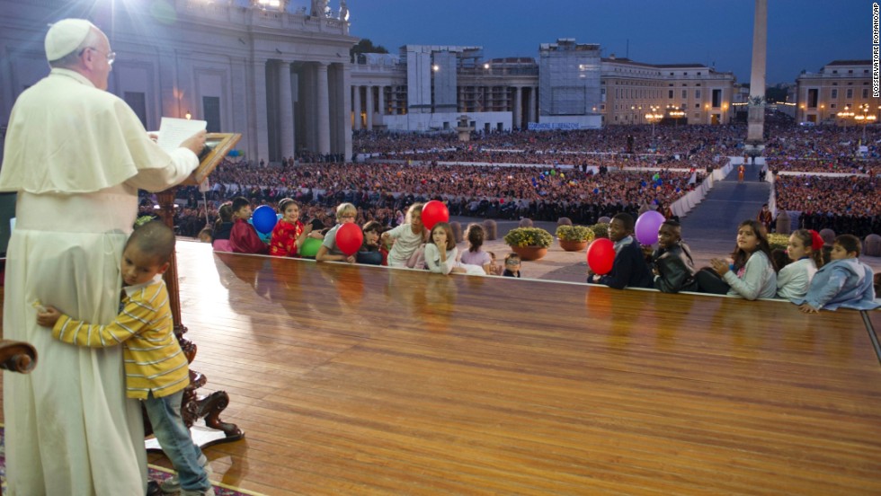 A young boy hugs Francis as he delivers a speech in St. Peter's Square in October 2013. The boy, part of a group of children sitting around the stage, played around the Pope as the Pope continued his speech and occasionally patted the boy's head. 
